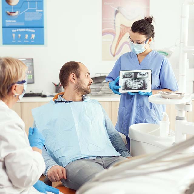 sick-man-sitting-stomatological-chair-listening-doctor-while-looking-tablet-dental-clinic sick-man-sitting-stomatological-chair-listening-doctor-while-looking-tablet-dental-clinic